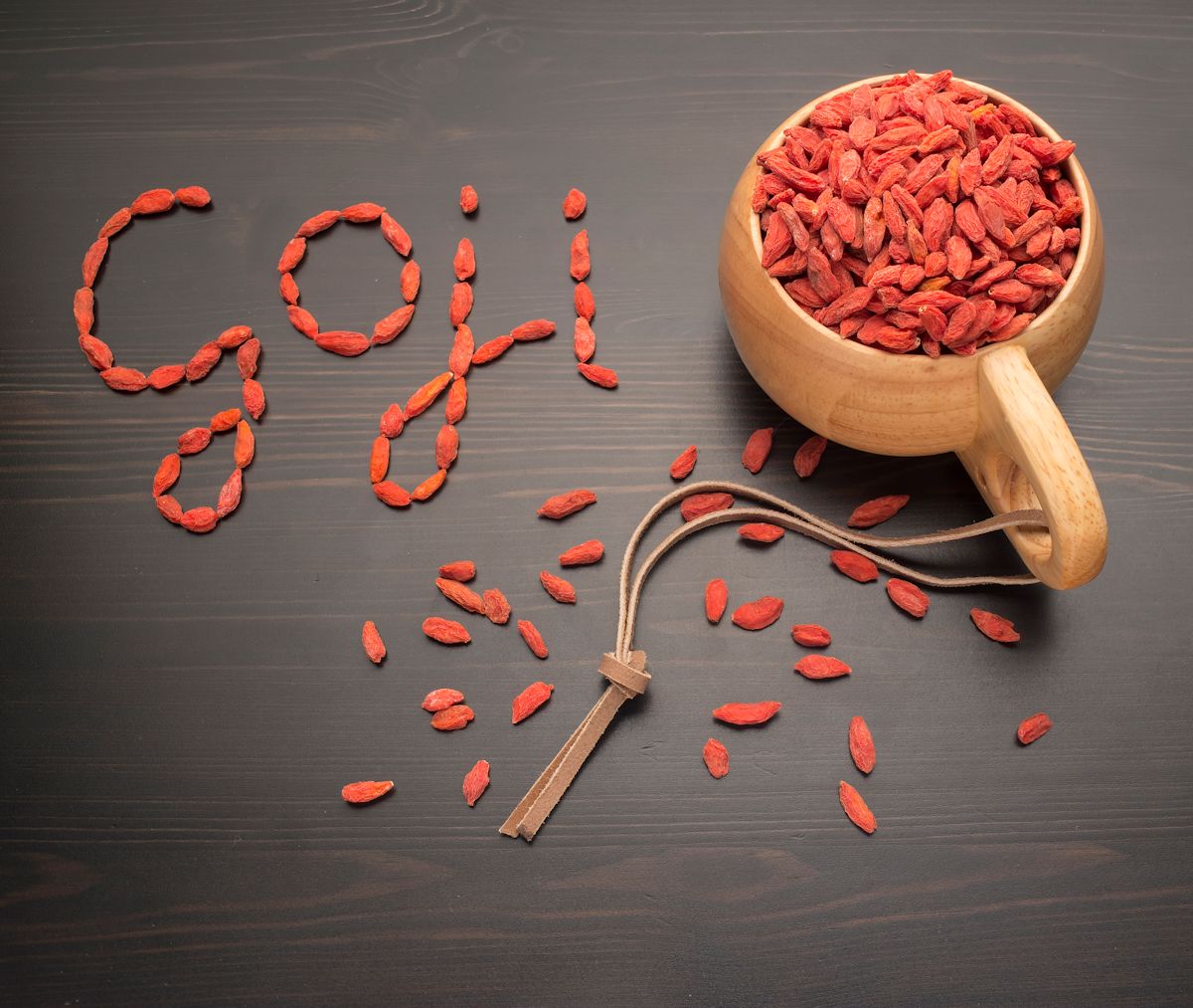 Caption goji berries on a black table next to a cup filled