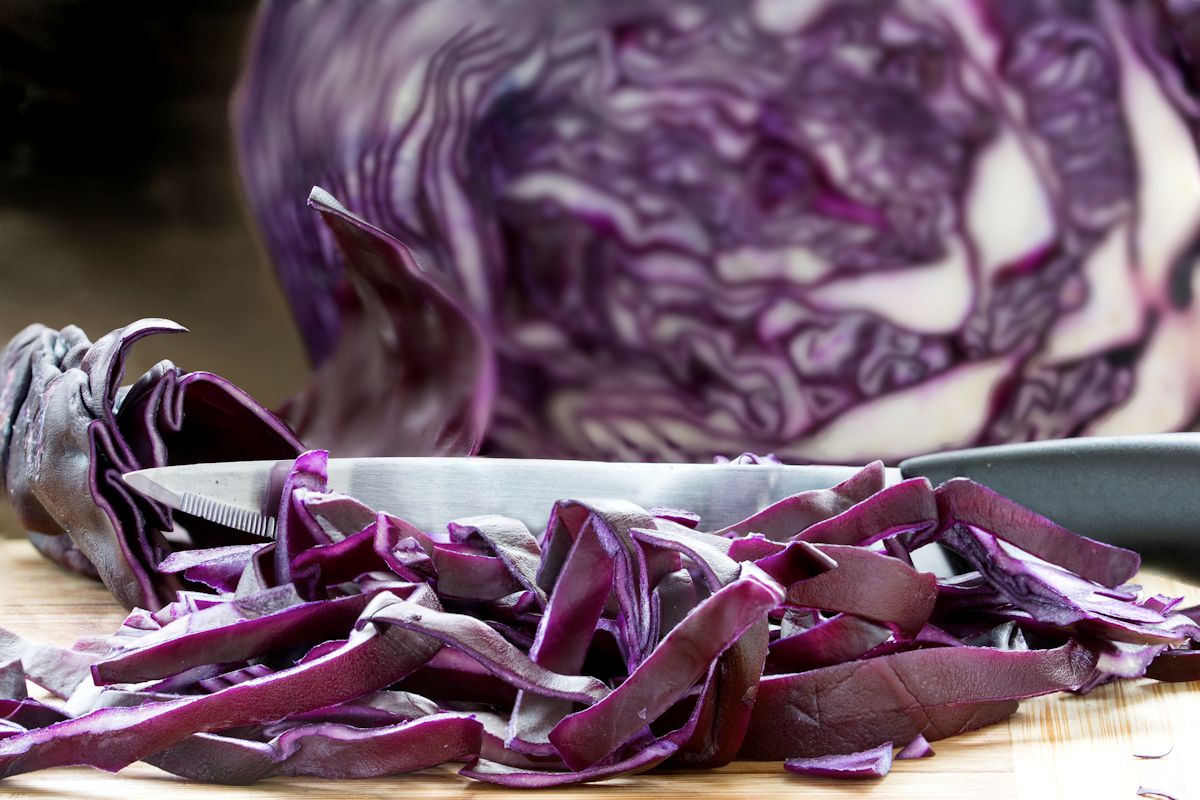 Cutting red cabbage into fine strips on a wooden board